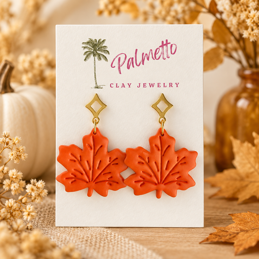 Orange polymer clay maple leaf earrings with embossed vein details and geometric gold-tone posts.