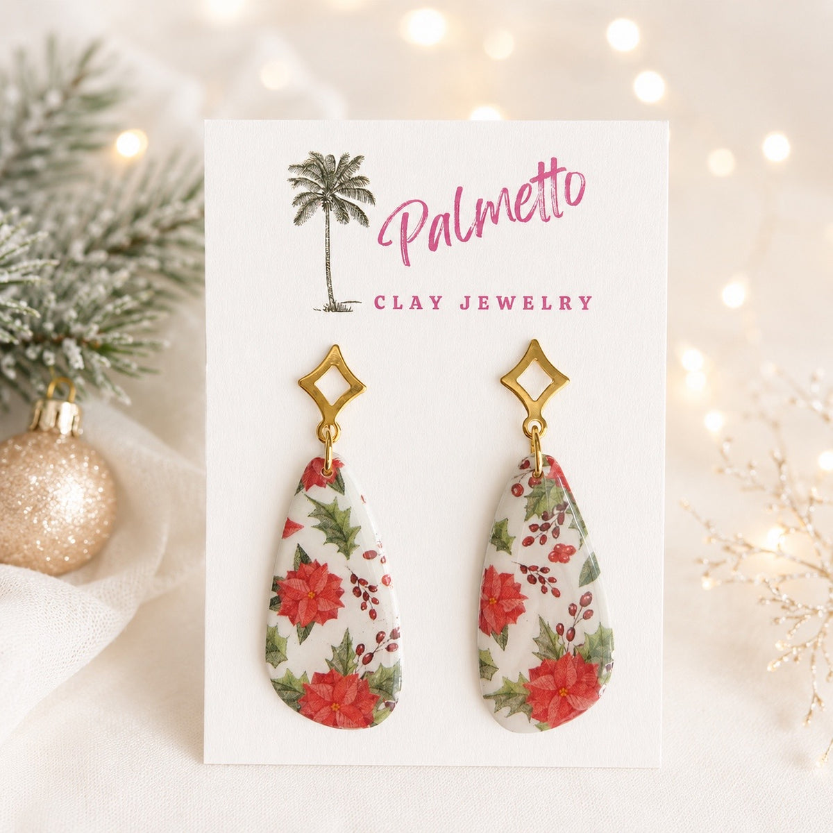 Handcrafted polymer clay Christmas earrings with red poinsettias, green holly leaves and berries on white teardrop shapes with gold-tone geometric studs.